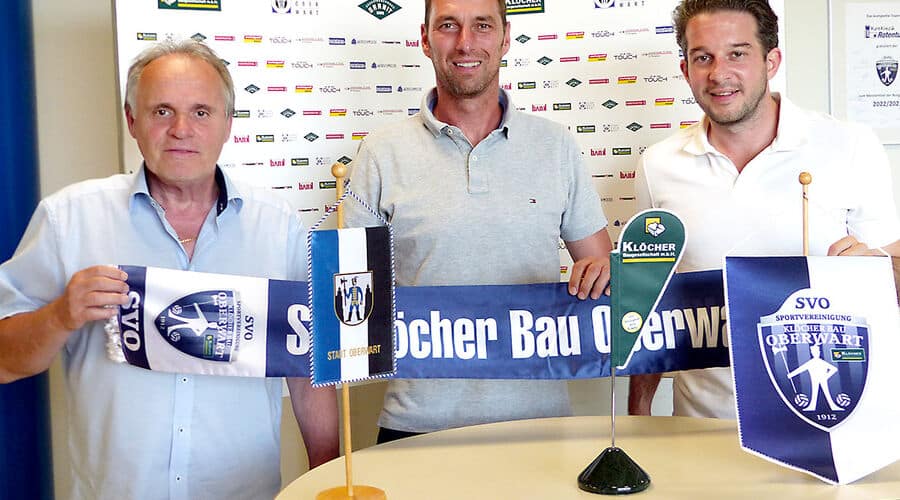 Drei Männer präsentieren ein Banner des SVO Klöcher Bau Oberwart mit Vereinslogo und Sponsorenlogos im Hintergrund.