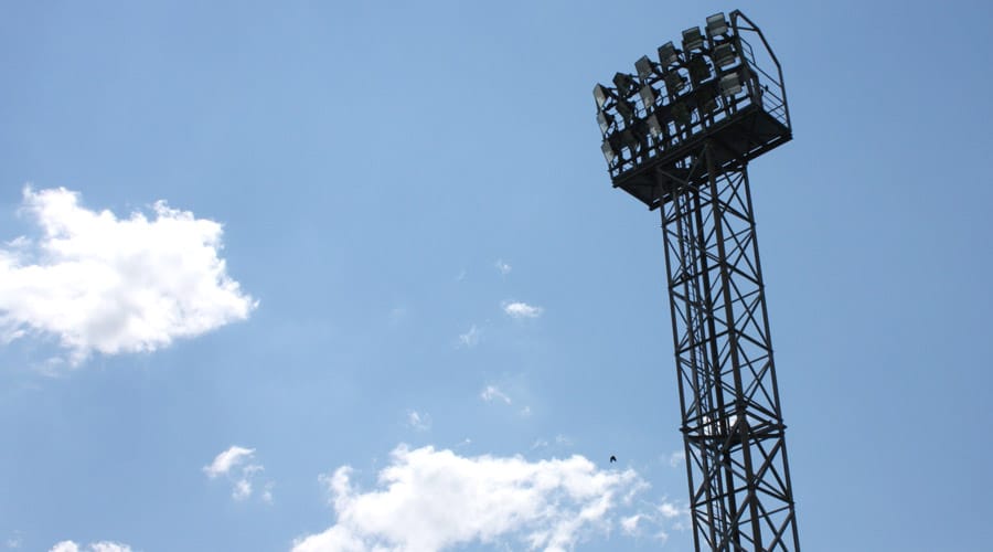 Flutlichtmast gegen blauen Himmel mit Wolken, ideale Outdoor-Beleuchtung für Sportveranstaltungen oder Stadien.