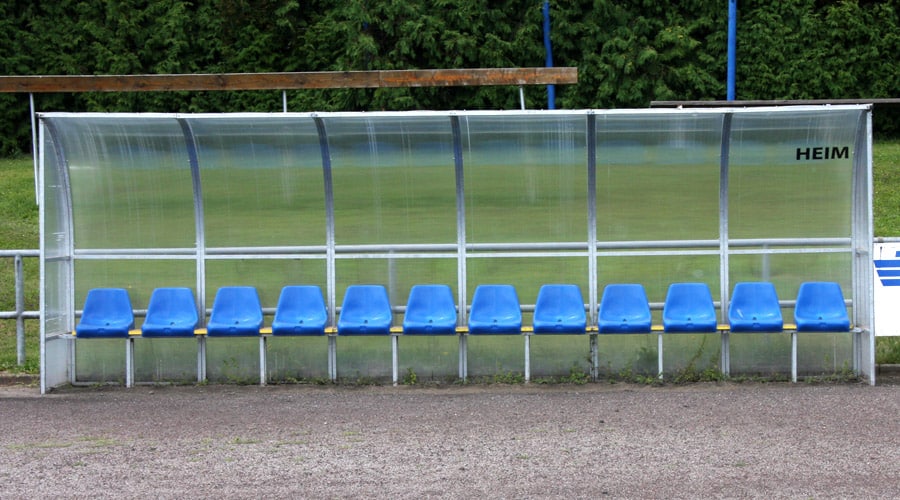 Leere Ersatzbank mit blauen Sitzen auf einem Fußballplatz. Ideal für Heimspiele und Teamvorbereitungen.