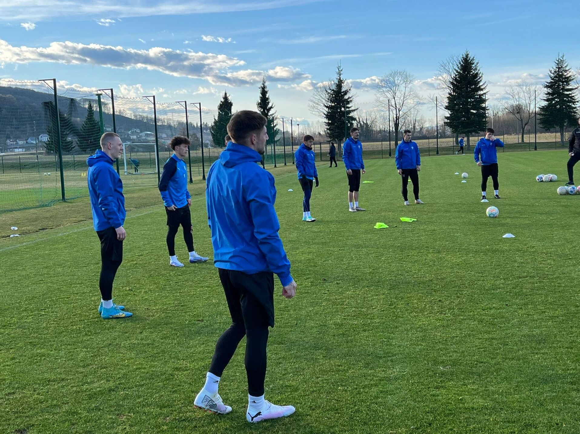 Fußballspieler im blauen Trainingstrikot beim Aufwärmen auf grünem Rasenplatz an einem klaren Tag.
