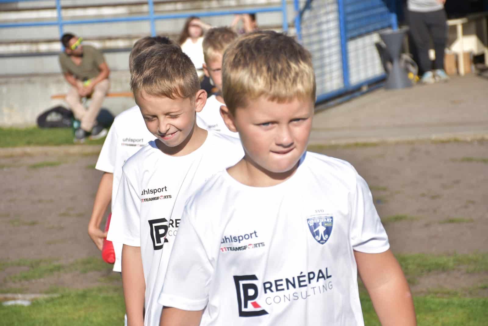 Junge Fußballspieler im weißen Trikot auf dem Spielfeld am sonnigen Tag, lächelnd und konzentriert.