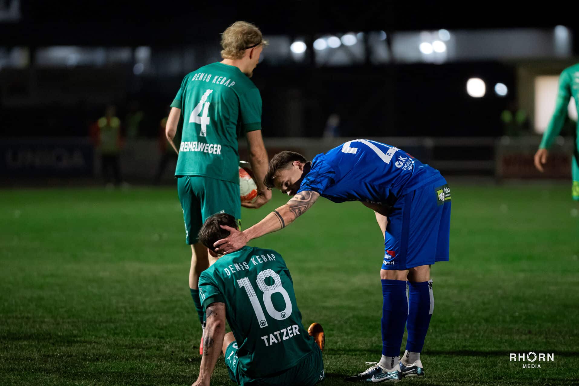 Fußballspieler trösten sich auf dem Feld bei Nachtspiel, Teamkameradschaft im Vordergrund.
