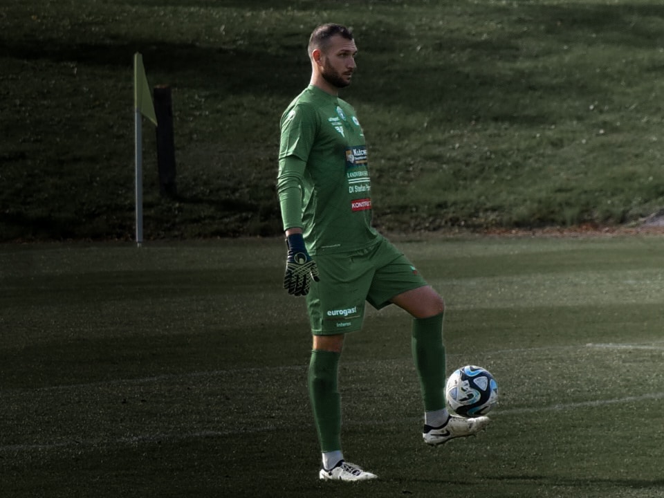 Fußballtorwart in grünem Trikot hält den Ball auf dem Spielfeld. Bereit für die nächste Aktion.