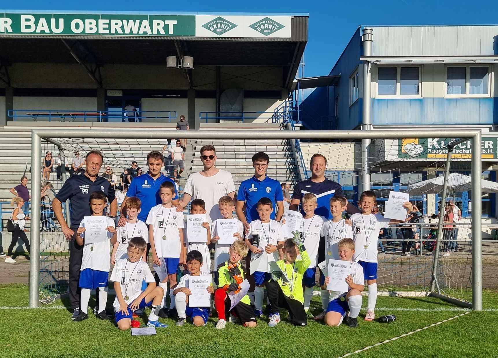 Jugendfußballteam mit Trainern und Urkunden im Stadion von Oberwart (U10), Gruppenbild mit Pokal und Medaillen.