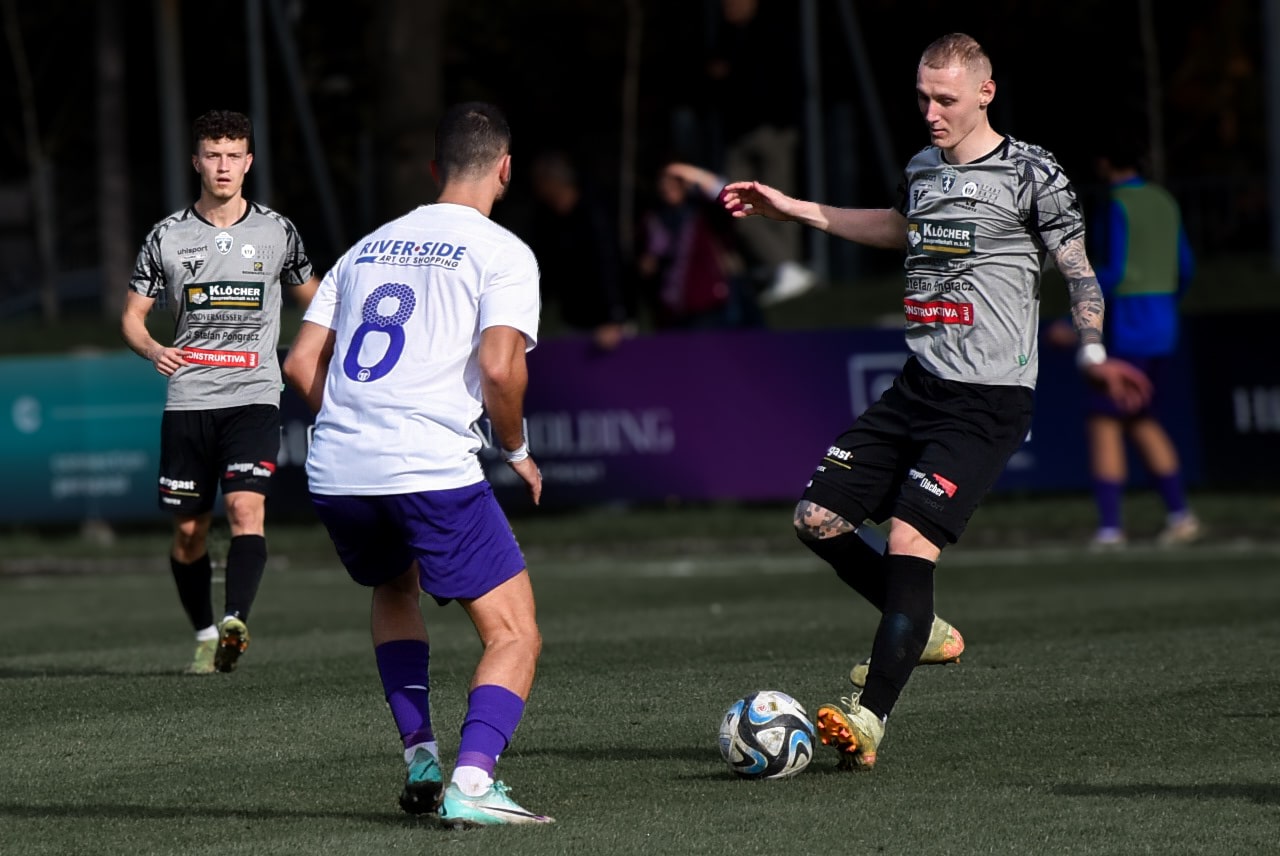 Fußballspiel in Aktion: Spieler in weißen und grauen Trikots kämpfen um den Ball, dynamische Spielszene.