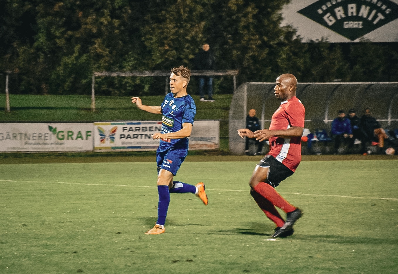 Zwei Fußballspieler im intensiven Zweikampf auf dem Spielfeld bei Nacht.