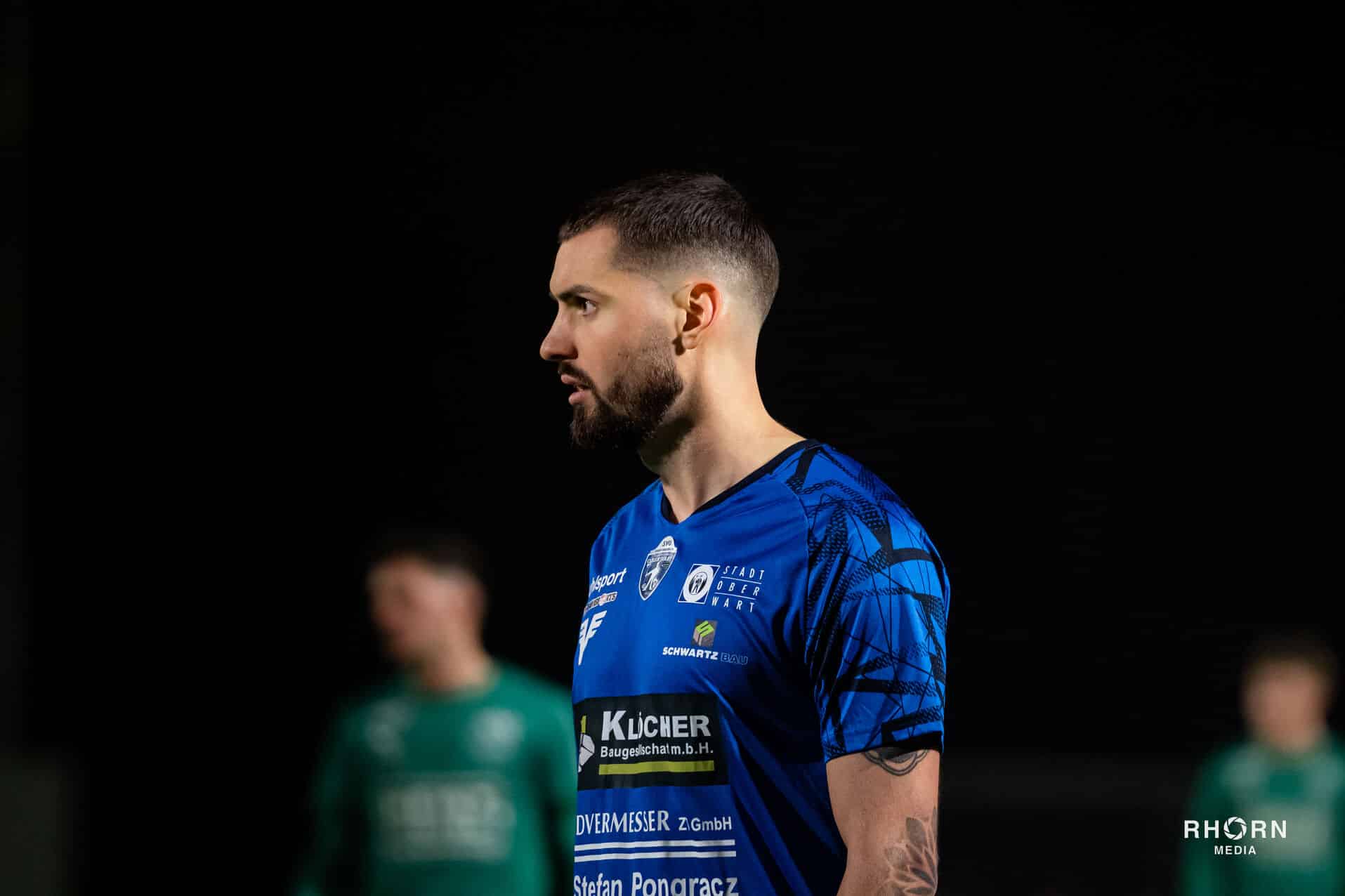 Ein Fußballspieler im blauen Trikot konzentriert sich während eines Spiels bei Nacht im Stadion.