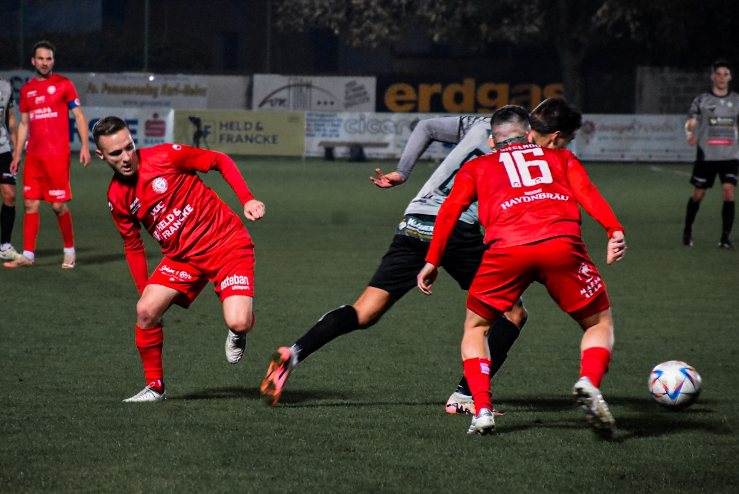 Fußballspiel in Aktion: Spieler kämpfen energisch um den Ball bei einem nächtlichen Match auf dem Spielfeld.