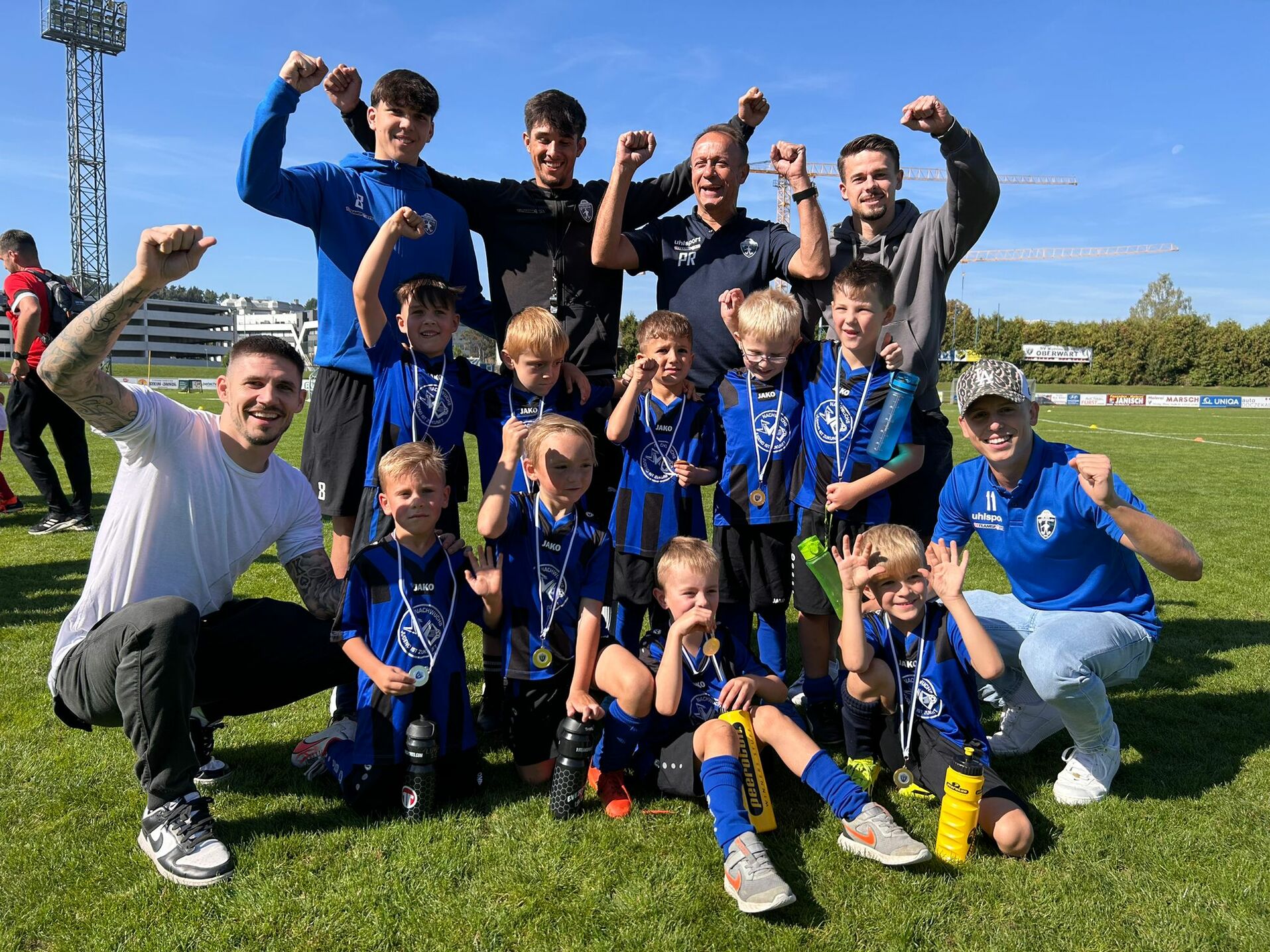 Kinderfußballteam feiert Turniersieg, glücklich mit Medaillen und Trainern auf dem Fußballfeld. Teamgeist und Freude pur!