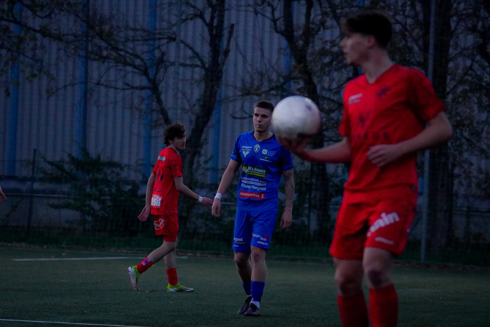 Fußball-Spieler in Rot und Blau auf dem Spielfeld beim Training oder Match im Freien bei Dämmerung.