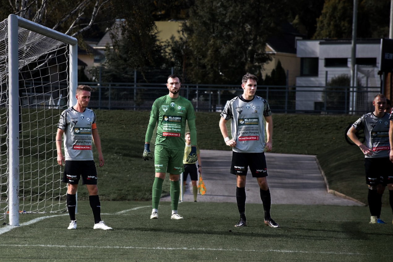 Fußballspieler am Torpfosten, bereit für Freistoß, in einem sonnigen Stadion, spannende Spielsituation.