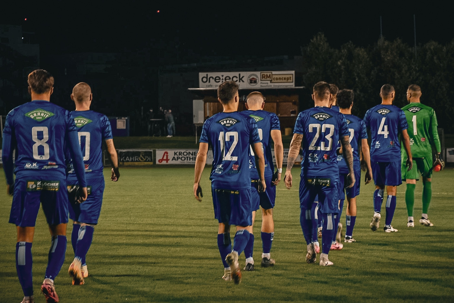 Fußballspieler in blauen Trikots auf dem Spielfeld bei Nacht, bereit für das Spiel. Sport, Teamgeist, Fußballmatch.