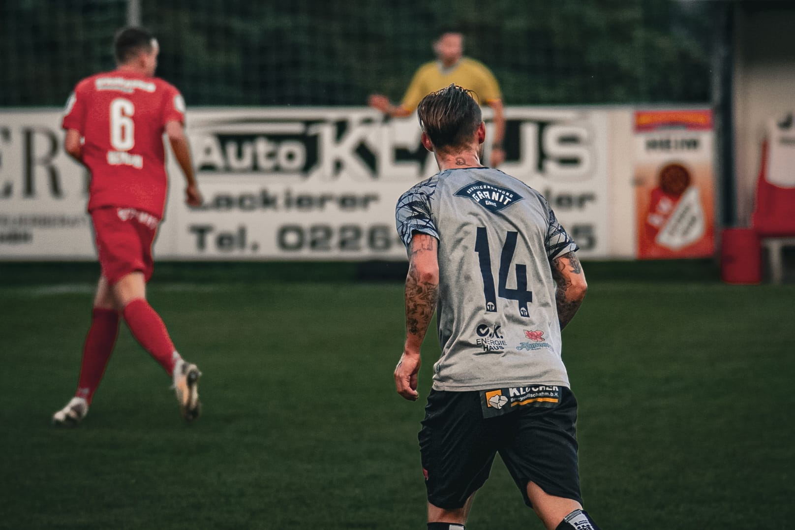 Fußballspieler während eines Spiels auf dem Feld in Aktion, trägt ein graues Trikot mit der Nummer 14.