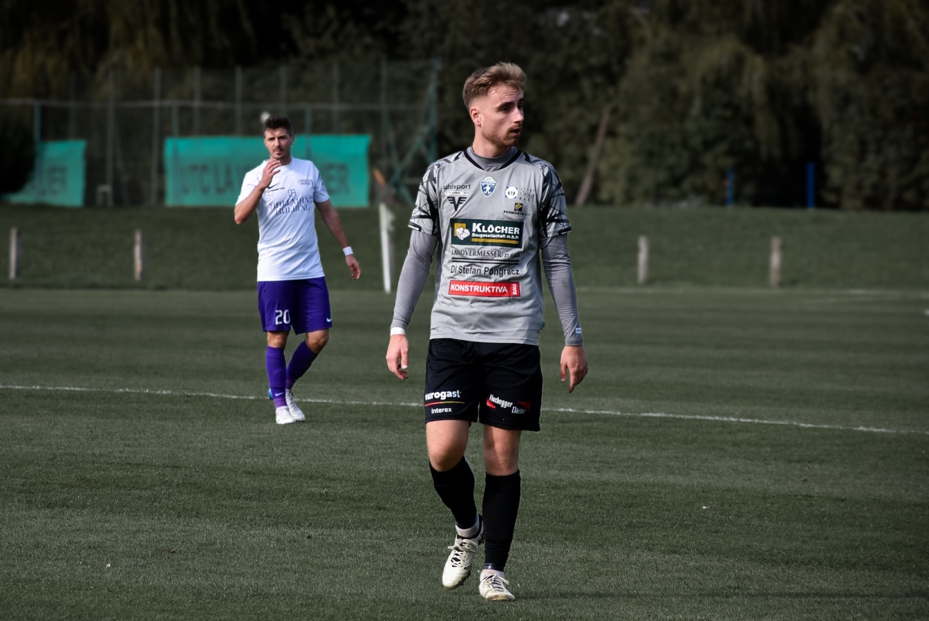 Fußballspieler in grauem Trikot während eines Spiels auf einem Fußballfeld im Freien.