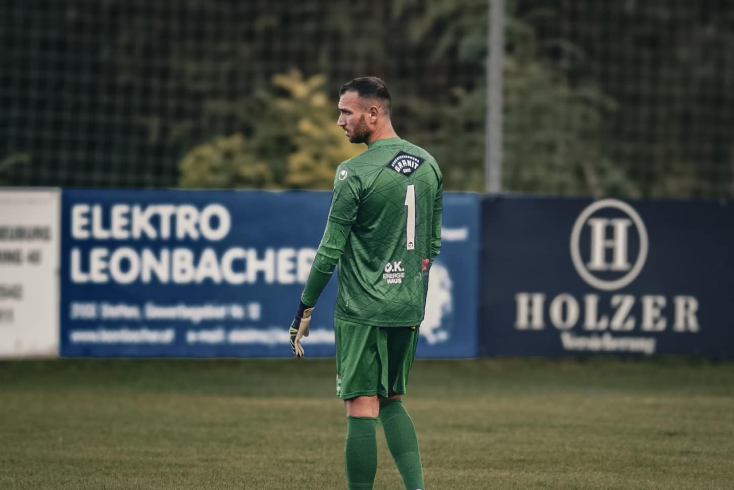 Fußballtorwart in grünem Trikot auf dem Spielfeld vor Werbebannern, Nummer 1 auf dem Rücken.
