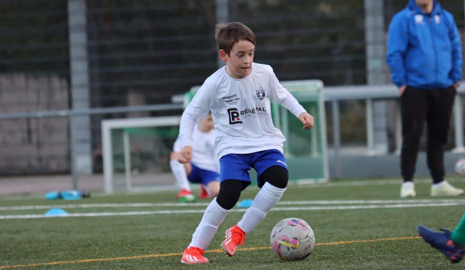 Junger Fußballer im weißen Trikot dribbelt auf dem Spielfeld, Training oder Jugendspiel im Freien.
