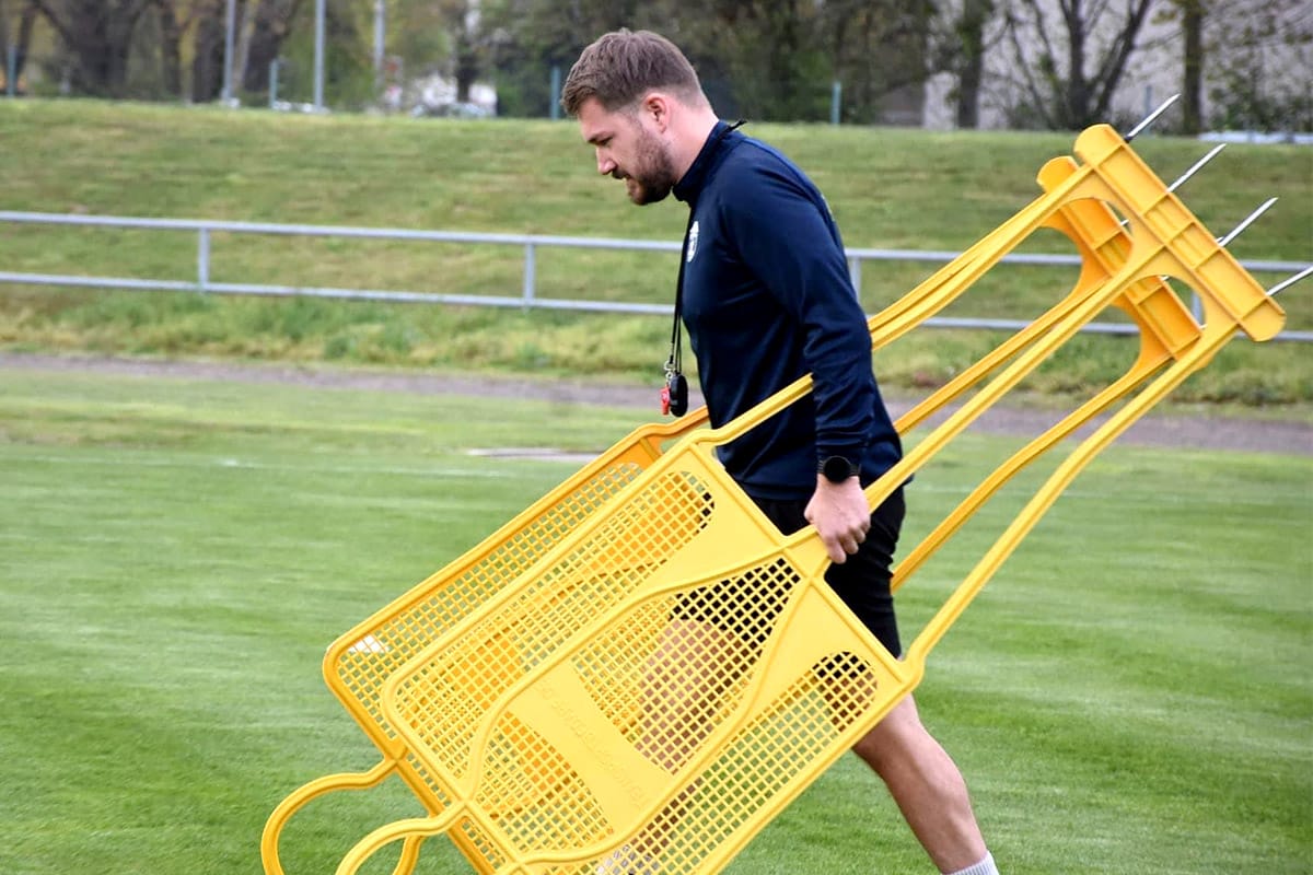 Trainer trägt gelbe Trainingsfiguren über den Sportplatz. Fußballtraining im Freien. Vorbereitung auf das nächste Spiel.