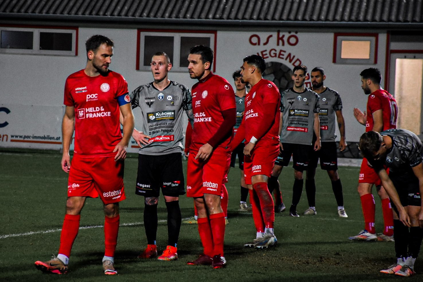 Fußballspieler in roten und grauen Trikots auf dem Spielfeld, bereit für das Spiel beim Abendtraining.