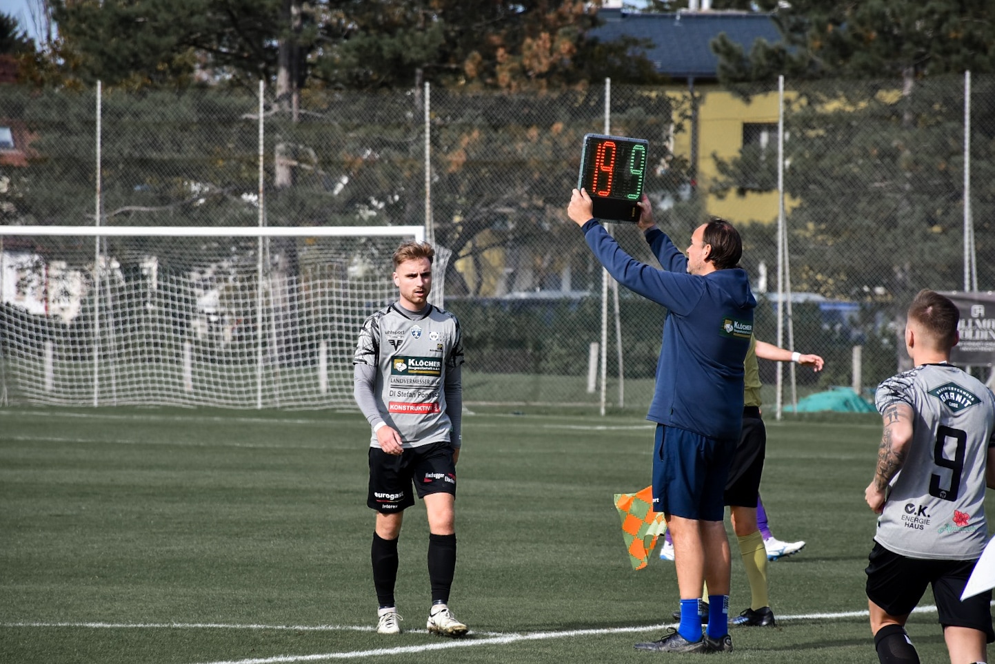 Fußballspieler bei Auswechslung auf dem Spielfeld, während der Schiedsrichter die Wechseltafel hochhält.