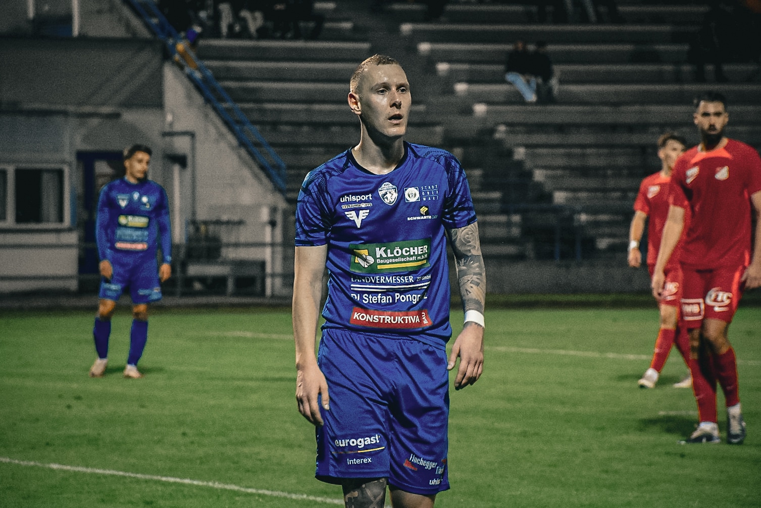 Fußballspieler in blauem Trikot auf dem Spielfeld während eines nächtlichen Spiels.