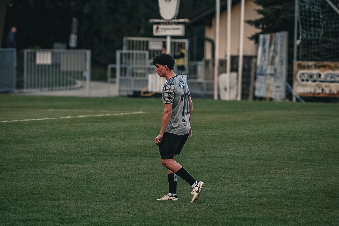 Fußballspieler auf dem Spielfeld während eines Spiels im Stadion, in grauem Trikot, seitlich fotografiert.