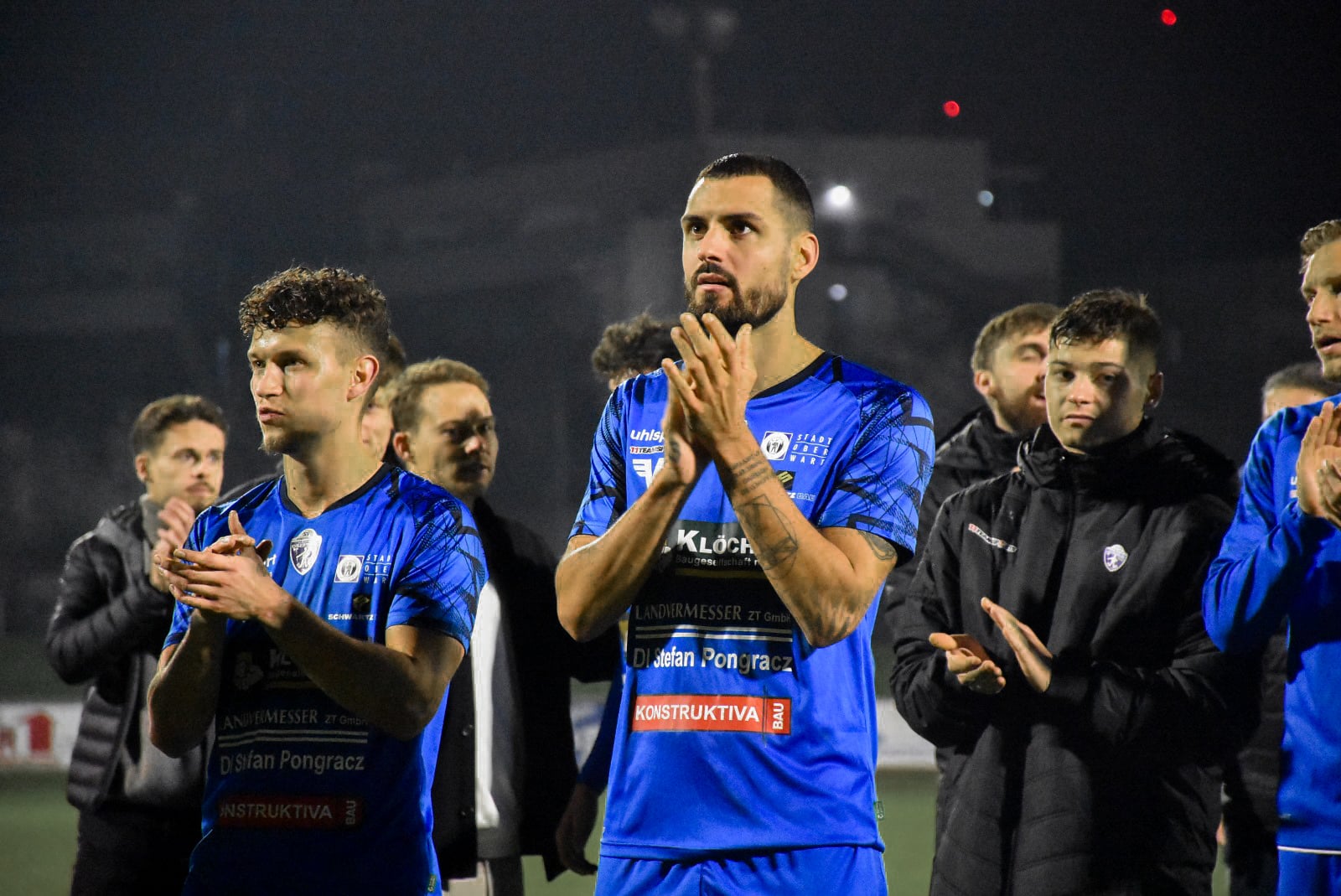 Fußballspieler im blauen Trikot nach einem Spiel, klatschen applaudierend auf dem Spielfeld.