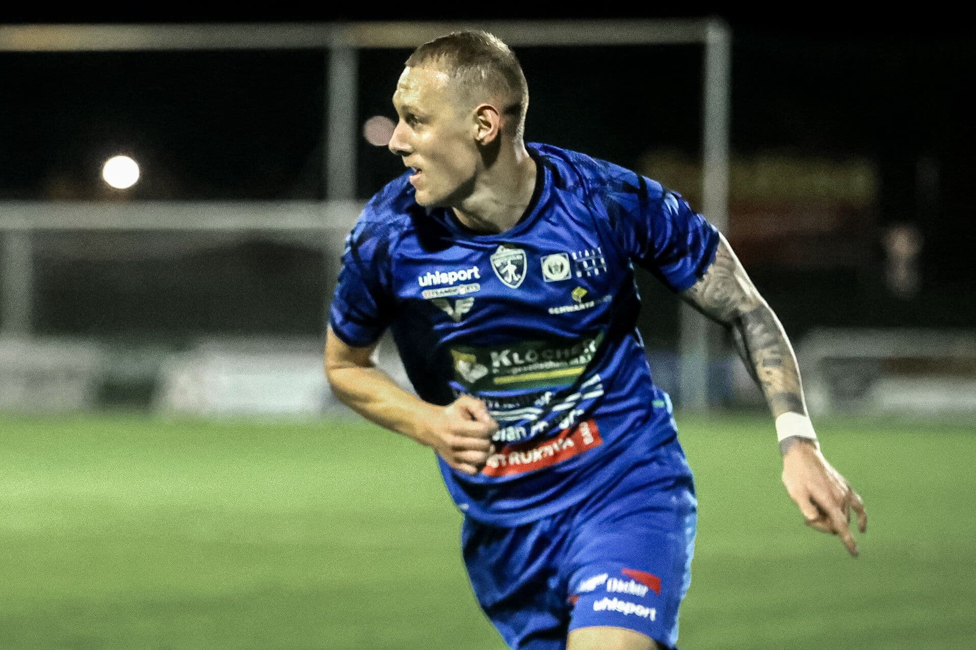 Fußballspieler im blauen Trikot, läuft auf dem Spielfeld, sportliche Aktion bei Nachtspiel.