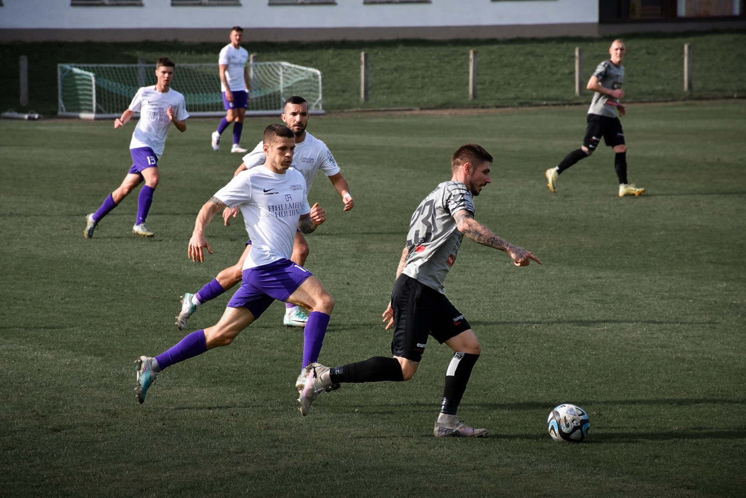 Fußballspiel auf Rasenplatz: Spieler im Kampf um den Ball, mit dynamischer Bewegung und intensiver Action.