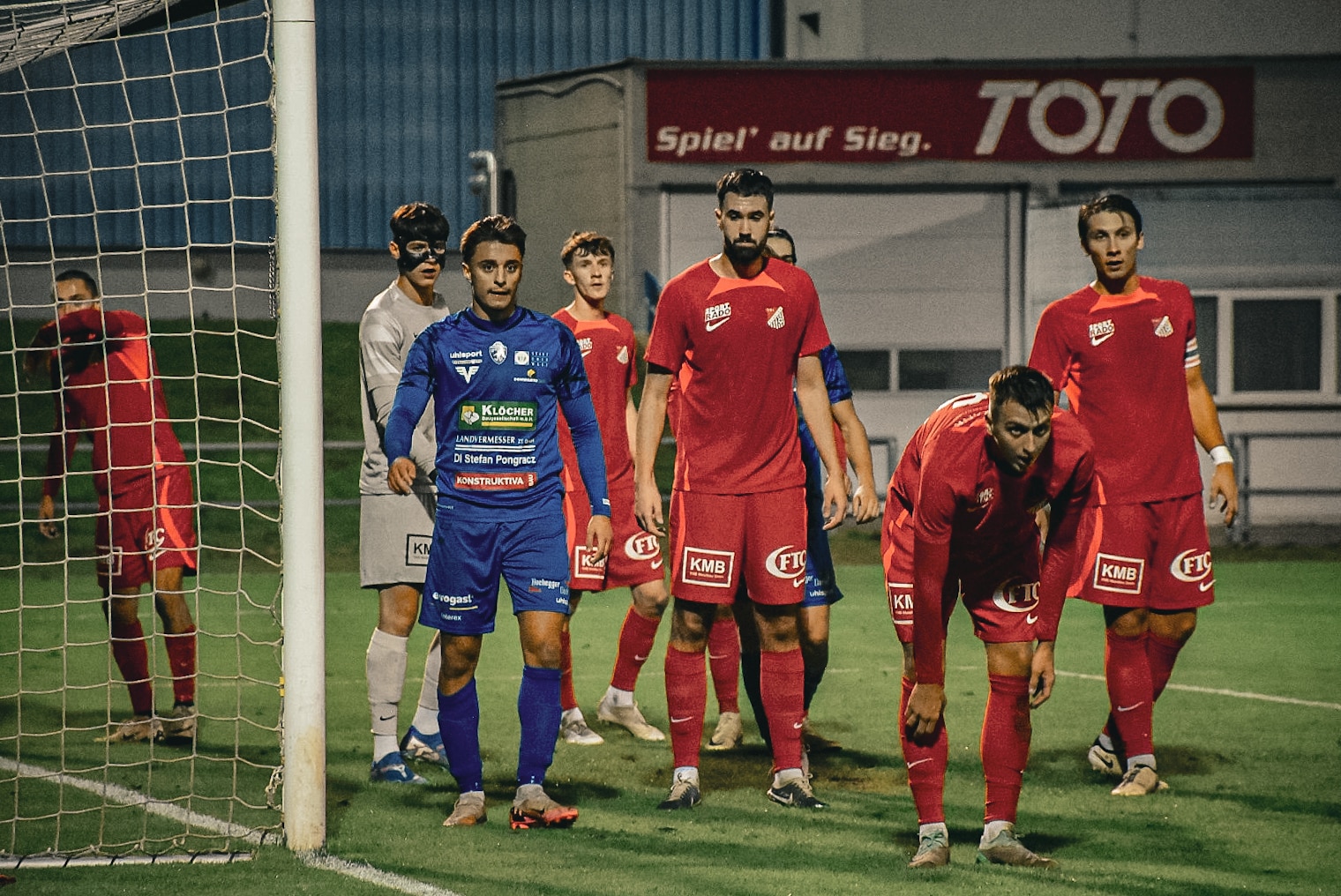 Fußballspieler bereiten sich in der Nähe des Tors auf einen Eckstoß vor, intensives Matchgefühl bei Nachtspiel.