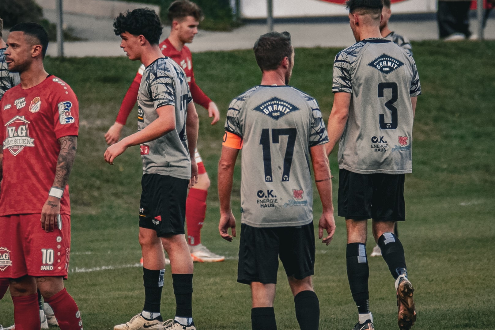 Fußballspieler auf dem Feld in roten und grauen Trikots, bereit für das Spiel. Rückansicht, sportliche Spannung.