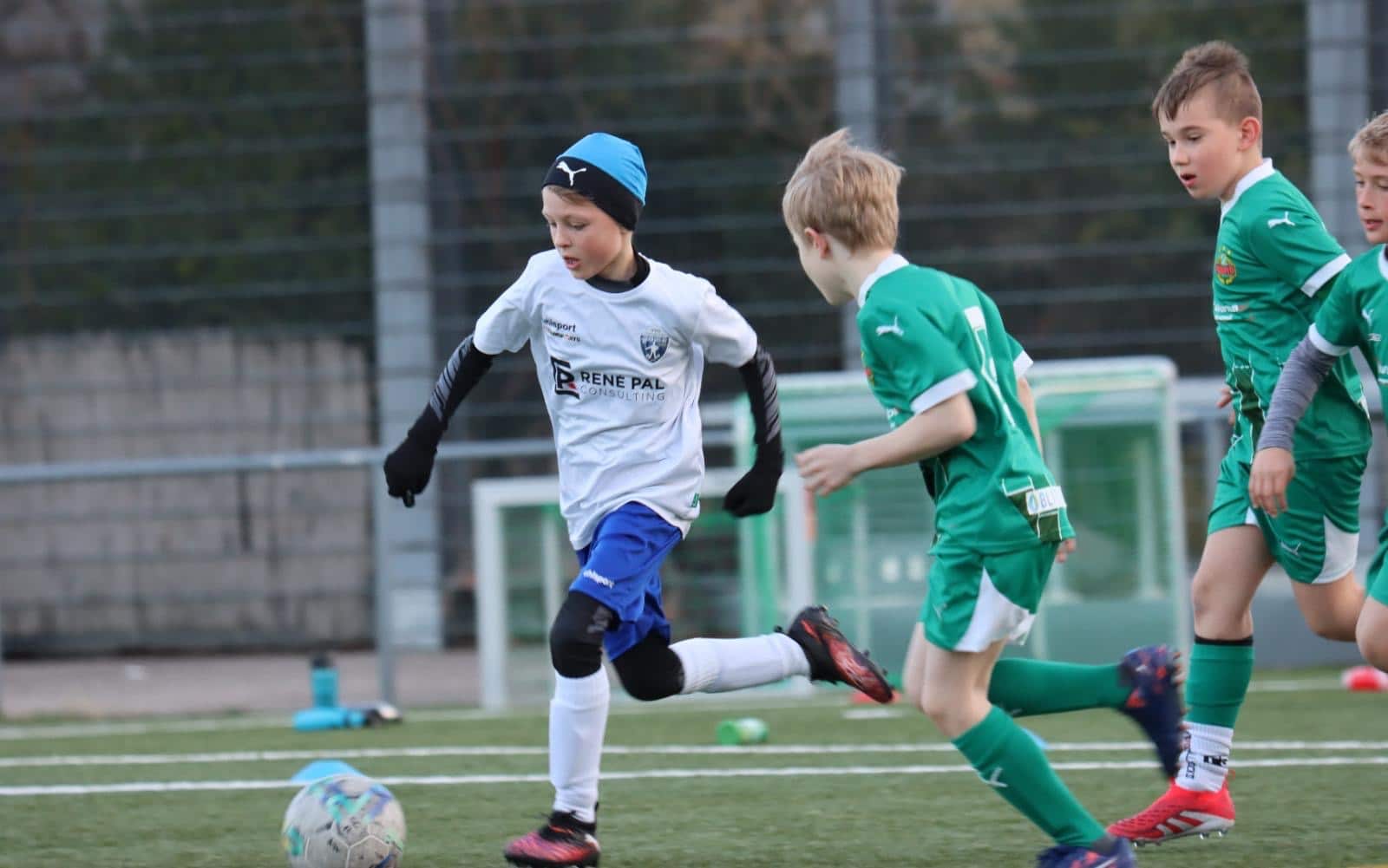 Kinder spielen Fußball auf einem Spielfeld, ein Spieler im weißen Trikot dribbelt den Ball.