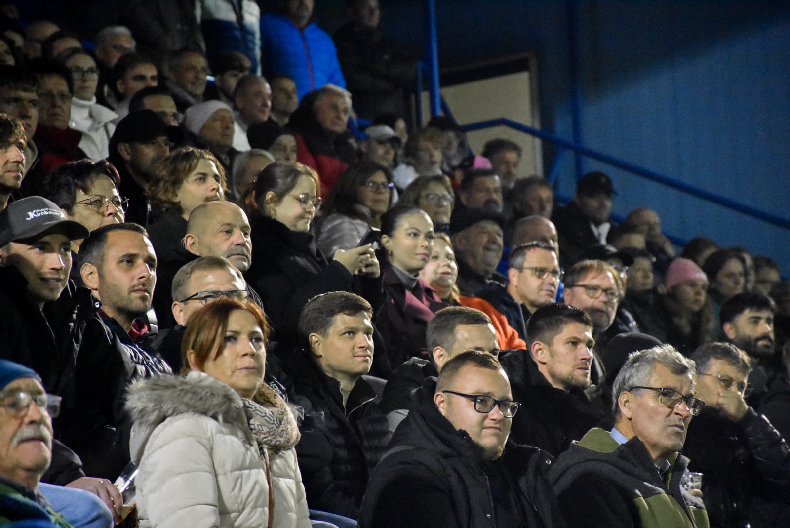Zuschauer im Stadion bei abendlichem Event, konzentriert und gespannt auf das Geschehen, Sitzreihen gut gefüllt.