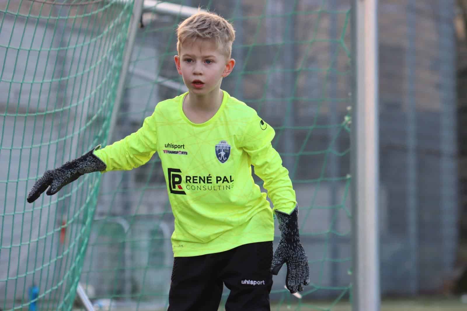 Junger Torwart mit neonfarbenem Trikot konzentriert im Fußballtor während eines Spiels.