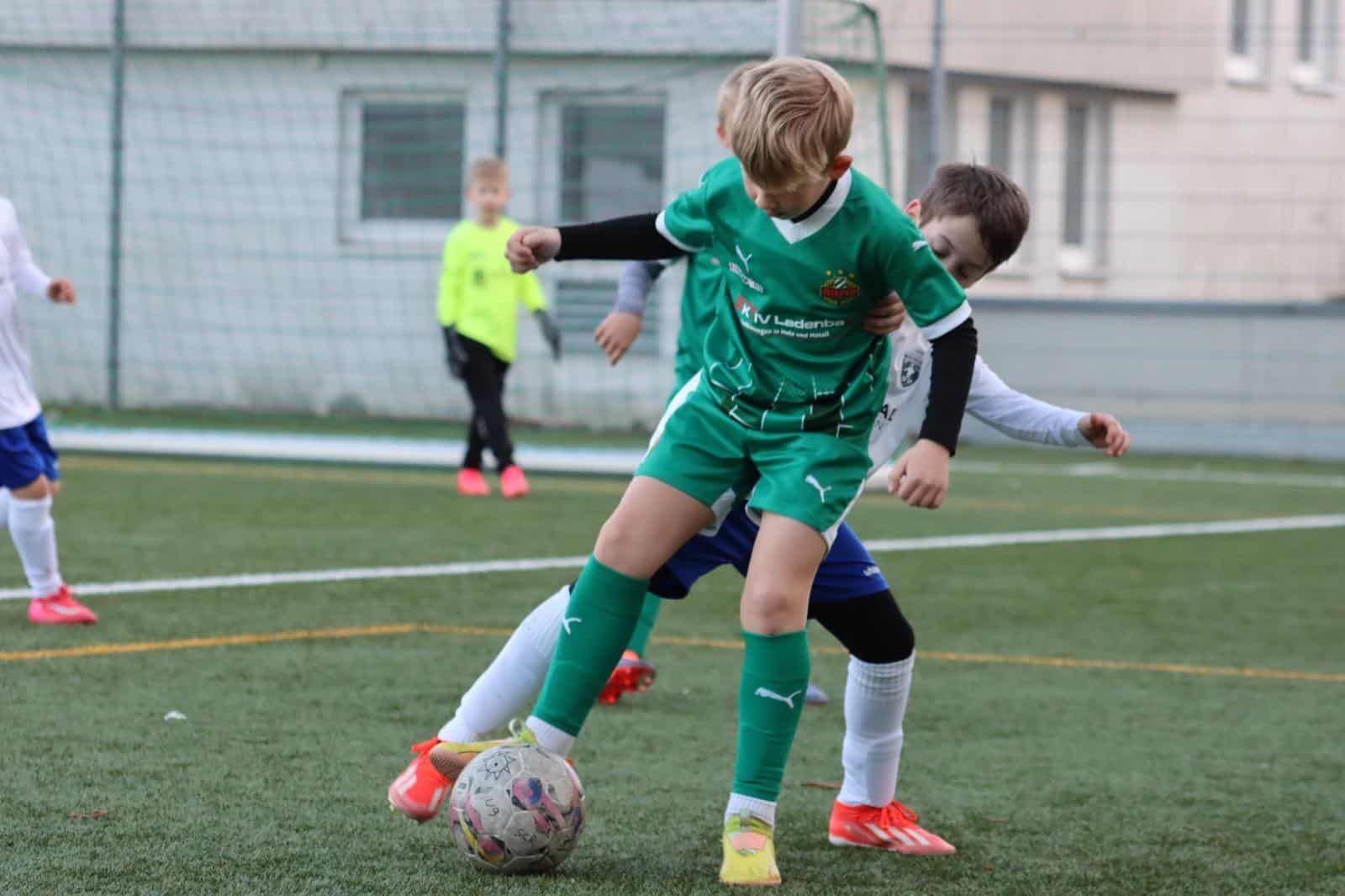 Kinder spielen begeistert Fußball auf einem Sportplatz im Freien.