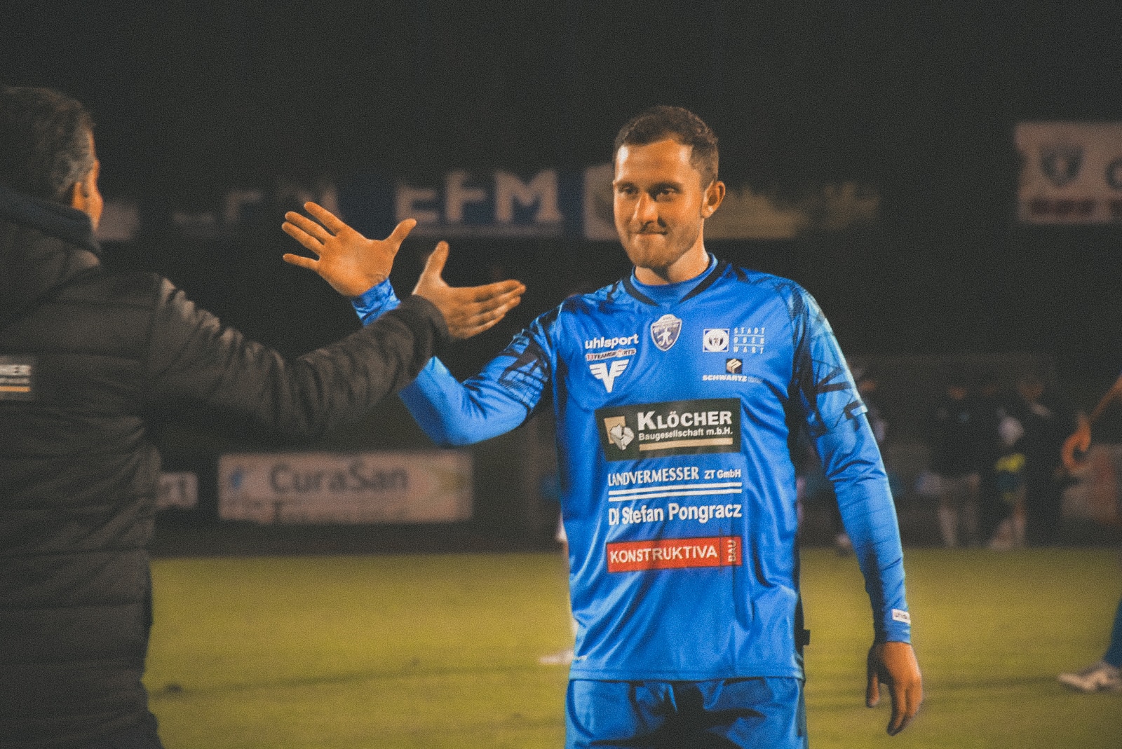 Fußballspieler im blauen Trikot gibt High-Five auf dem Spielfeld, Teamgeist, Nachtspiel, Feierlicher Moment.