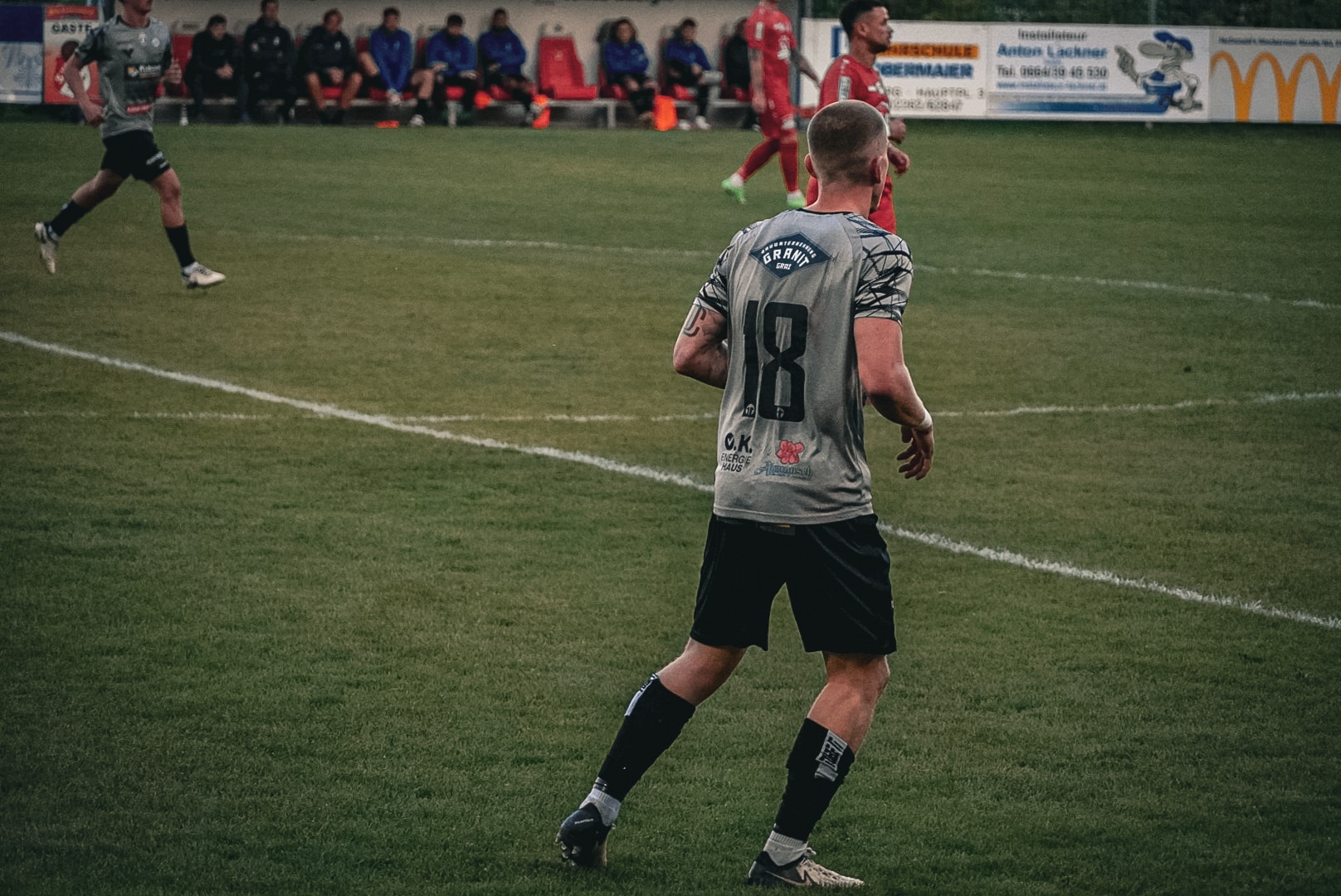 Fußballspieler mit Trikot Nummer 18 im Spiel auf dem Rasenplatz, Blick in Richtung Spielfeld, Mannschaft in Aktion.
