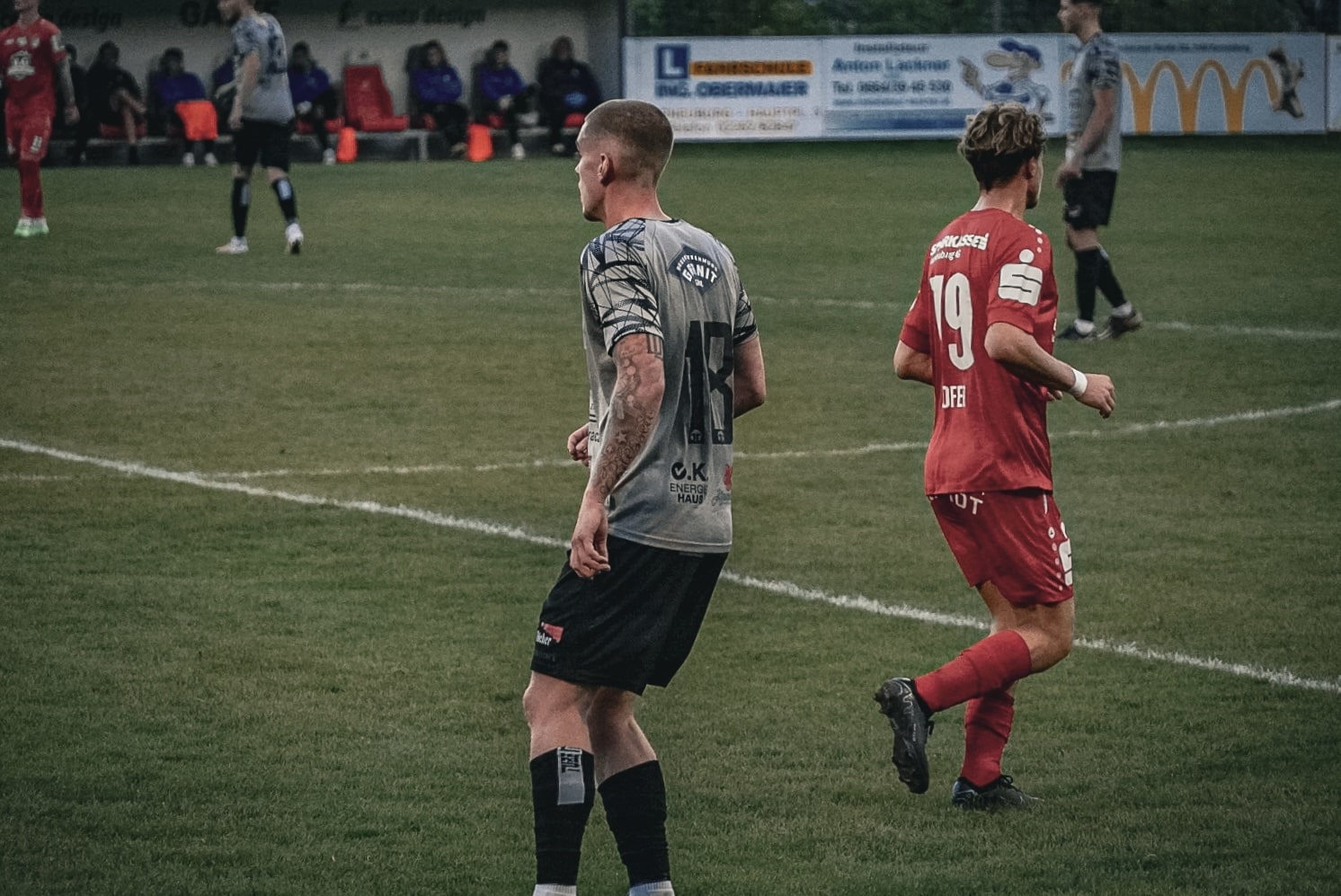 Fußballspiel in Aktion: Spieler in grau und rot auf dem Spielfeld konzentrieren sich auf den Ball.