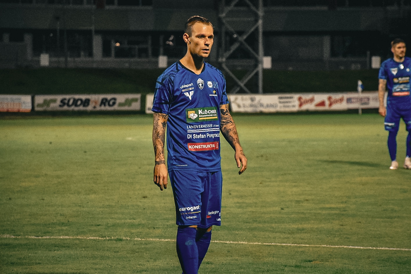 Fußballspieler im blauen Trikot auf dem Spielfeld beim nächtlichen Spiel, bereit für die nächste Aktion.