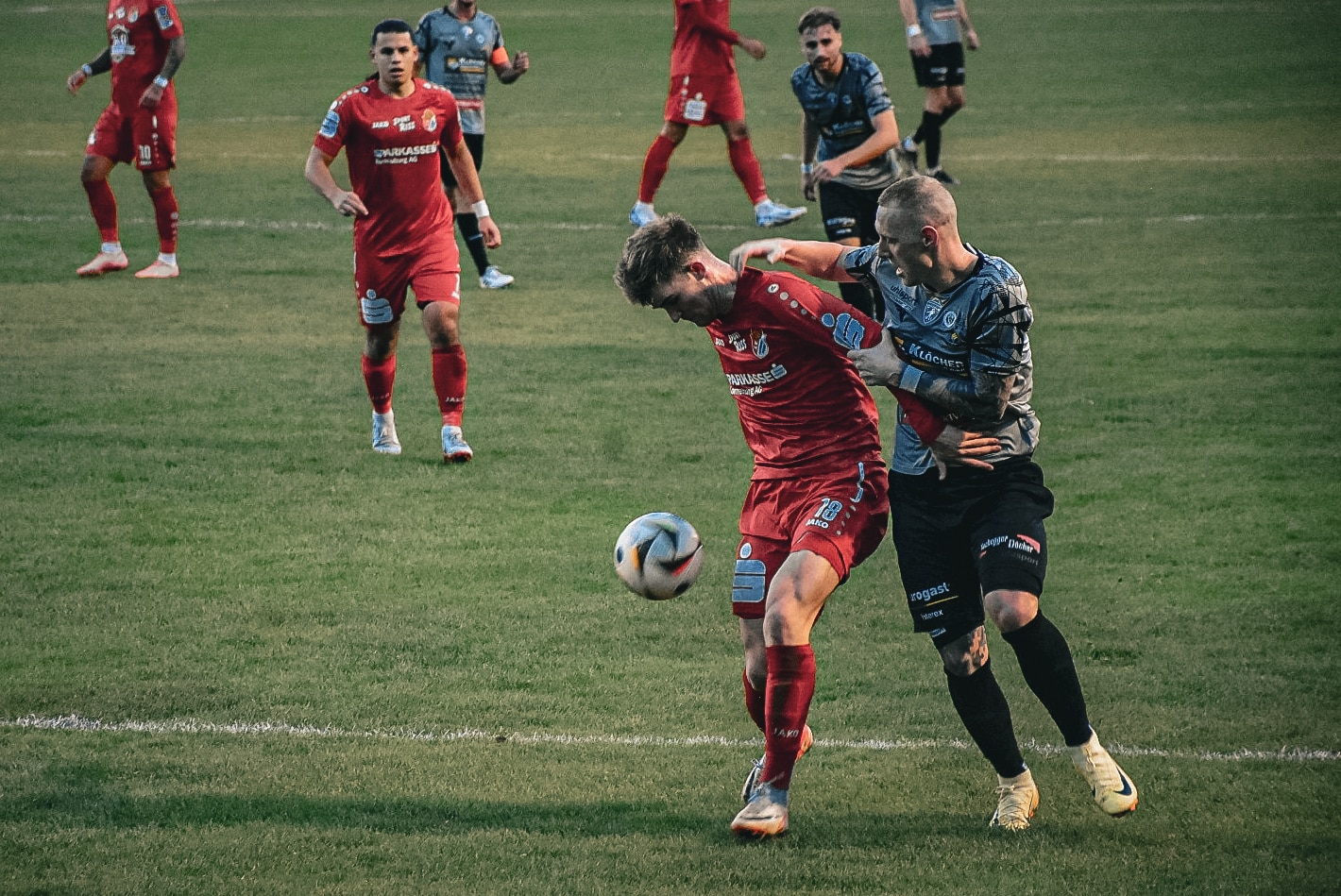 Fußballspieler im Zweikampf um den Ball während eines spannenden Spiels auf grünem Rasen.