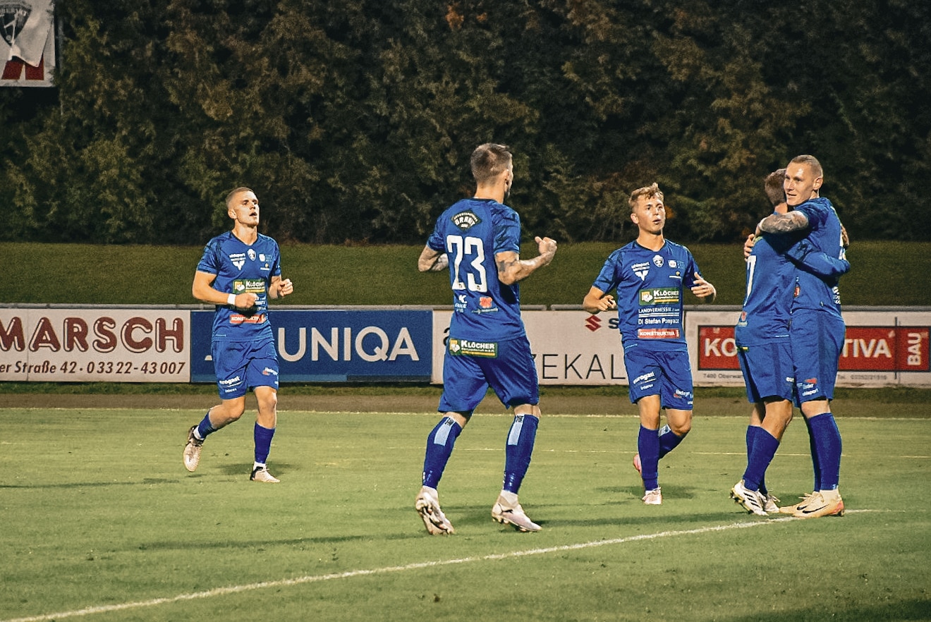 Fußballspieler in blauen Trikots feiern ein Tor auf dem Spielfeld. Spannung beim Fußballspiel am Abend.
