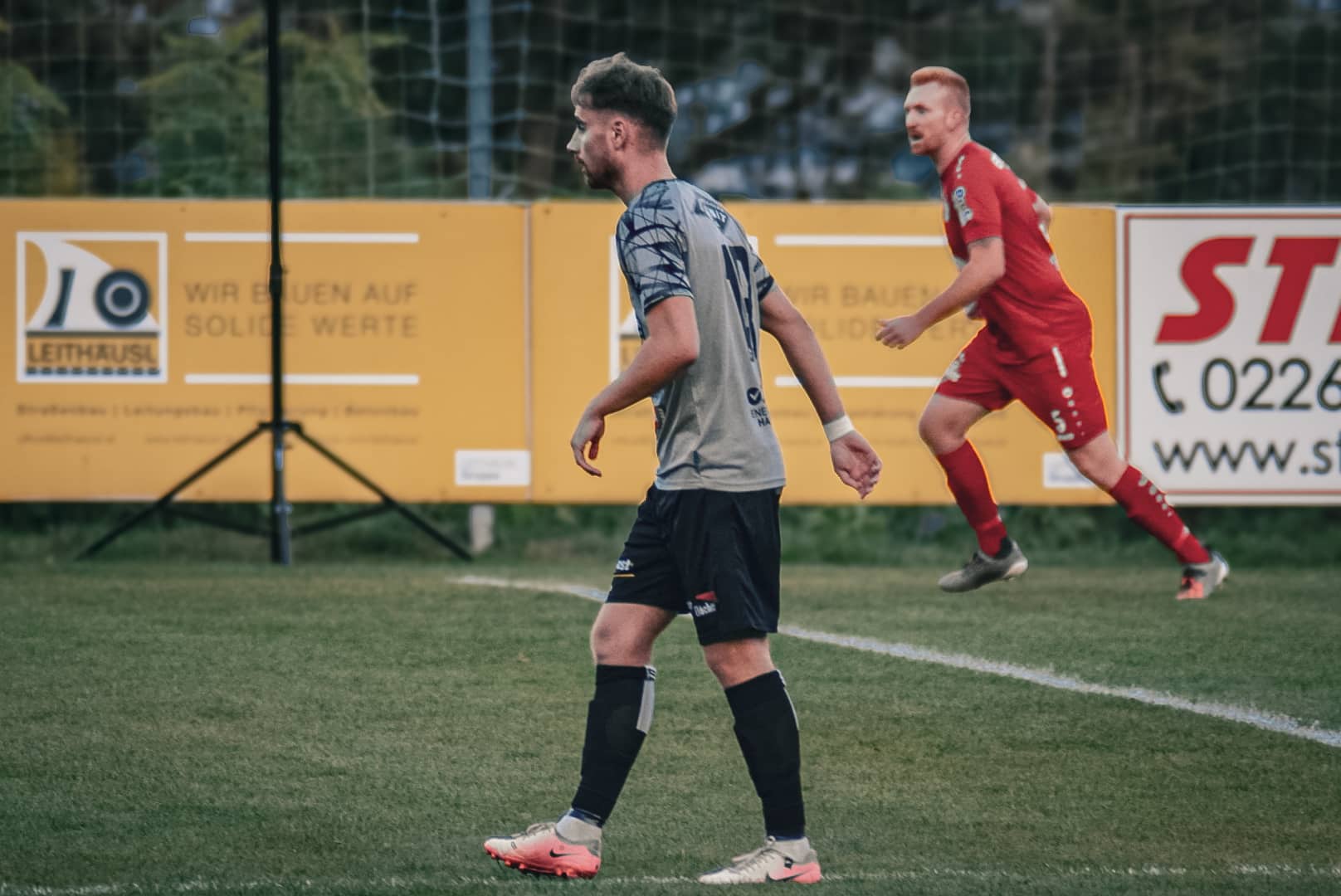 Fußballspieler in Aktion auf grünem Spielfeld vor Werbebannern während eines Spiels im Freien.
