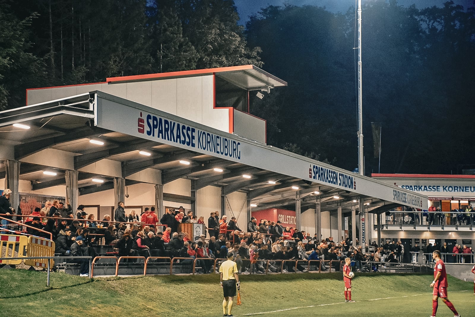 Stadionabendspiel in Korneuburg: Zuschauer verfolgen Fußballspiel unter Flutlicht im Sparkasse Stadion.