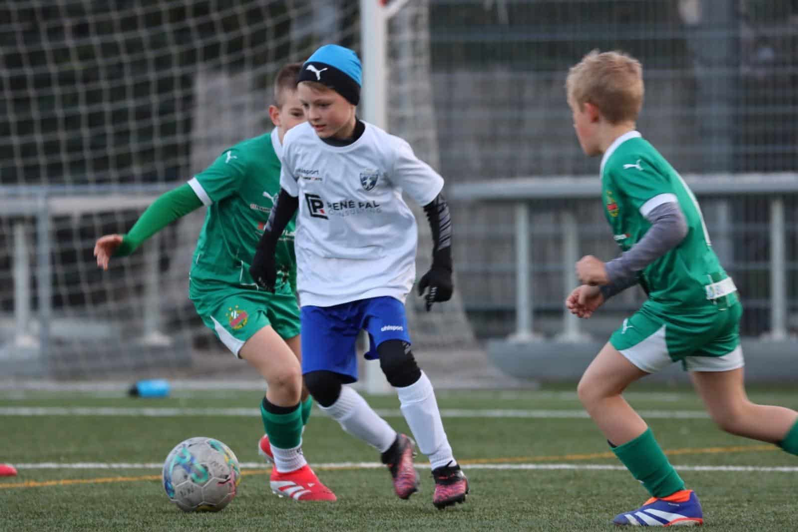 Junge Fußballer im Spiel, intensives Dribbling auf dem Spielfeld, Grün- und Weißtrikots, Kinderfußball im Freien.