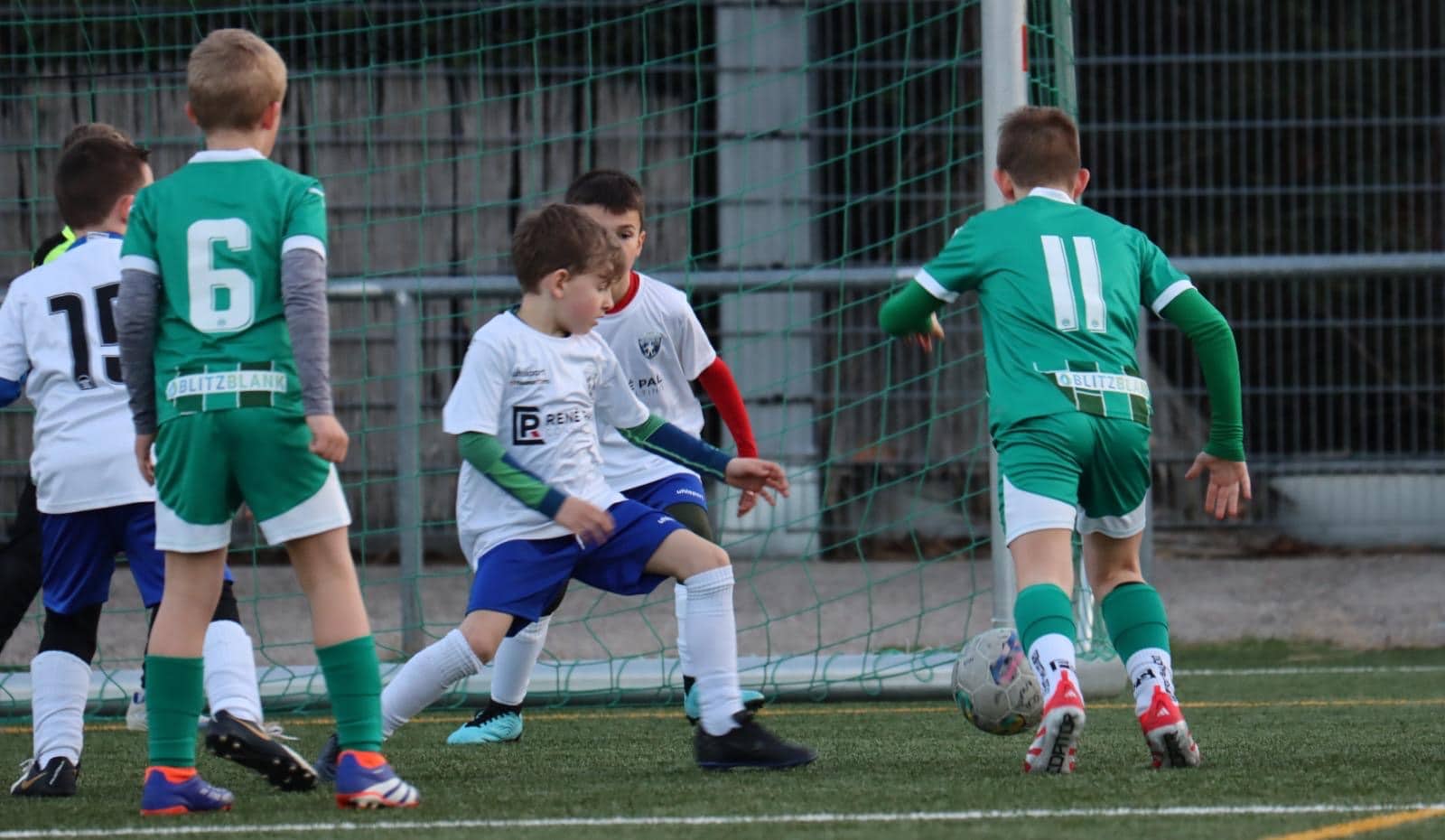 Kinder spielen Fußball im Stadion, Wettkampf zwischen grünem und weißem Team, Nahaufnahme vor dem Tor.