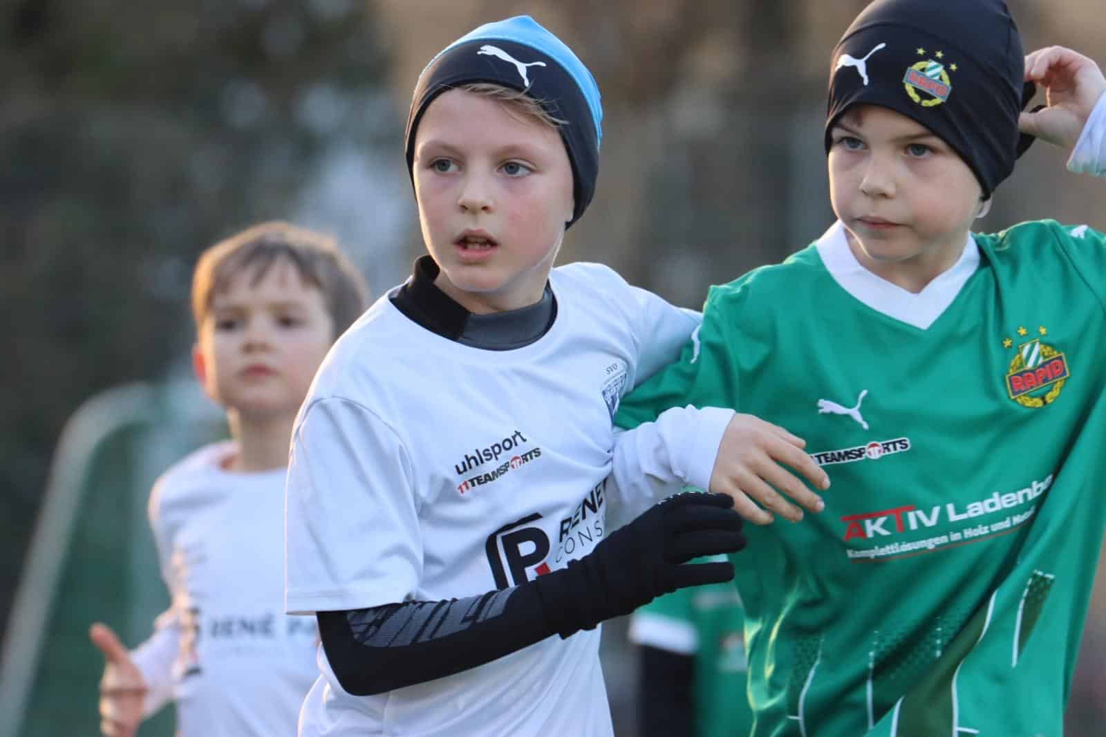 Junge Fußballspieler im Wettkampf mit weißen und grünen Trikots auf dem Spielfeld, dichtes Spielgeschehen.