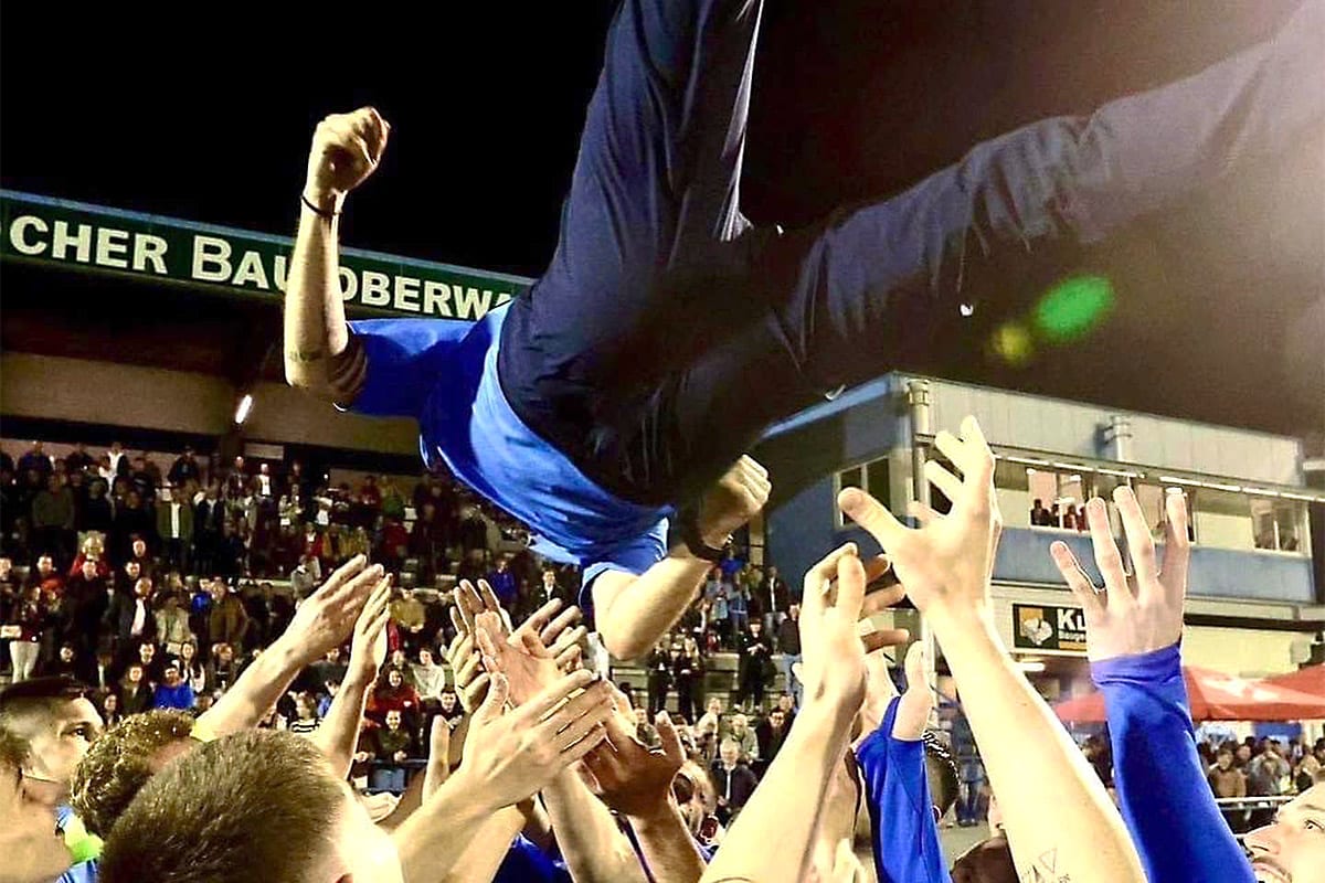 Fans feiern Spieler mit Luftwurf bei Fußballspiel in belebtem Stadion. Freude und Jubel in der Nacht.
