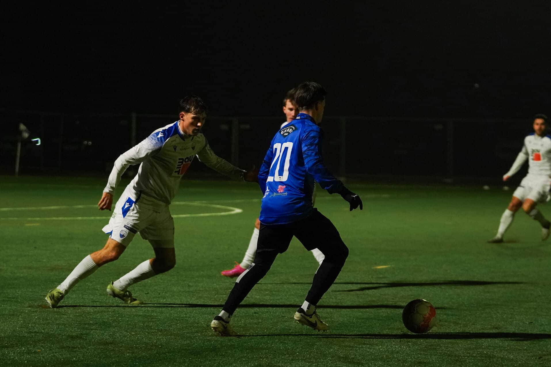 Fußballspiel bei Nacht: Spieler in Aktion auf dem Feld, dunkle Umgebung, spannend und dynamisch.