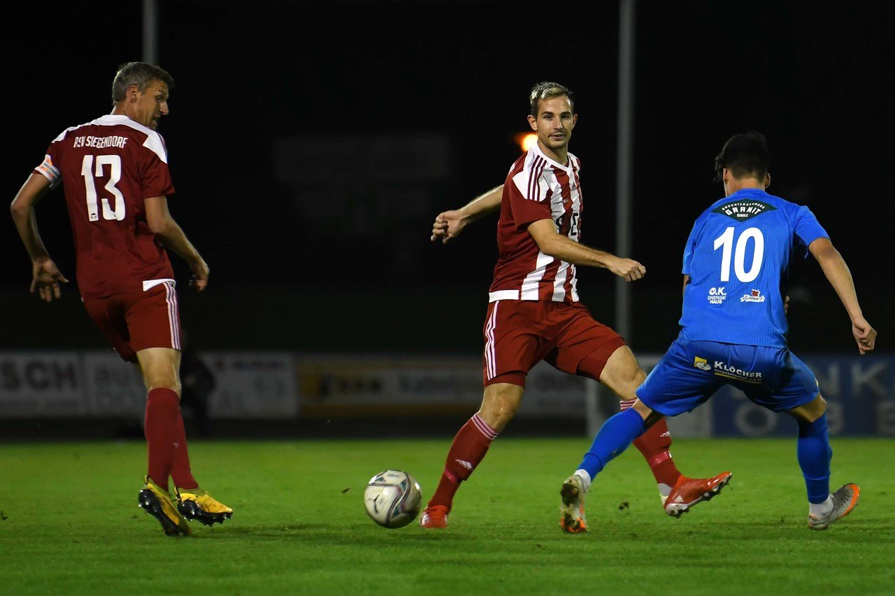 Zwei Fußballspieler in rot und blau kämpfen nachts auf dem Spielfeld um den Ball.