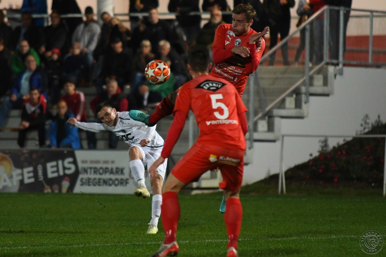 Fußballspiel mit intensiver Zweikampfszene im Mittelfeld zwischen zwei Teams in Rot und Weiß.
