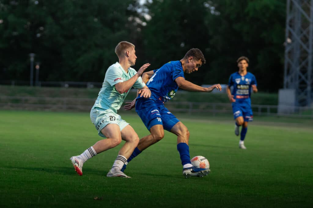 Zwei Fußballspieler im Zweikampf während eines Spiels auf grünem Rasen, konzentriert auf den Ball.